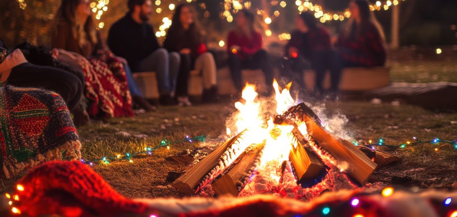 Ein Bild von einer Gruppe Jugendlicher, die um ein Lagerfeuer mit einem geschmückten Weihnachtsbaum und vielen Geschenken und Lichtern sitzen.